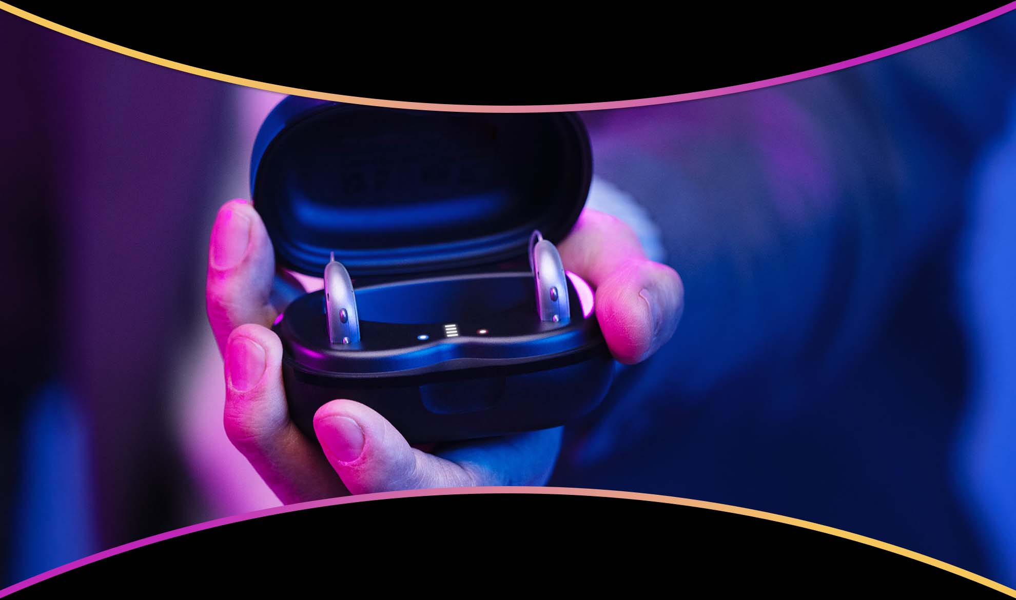 A hand holding an open charger with a pair of RIC hearing aids in it.